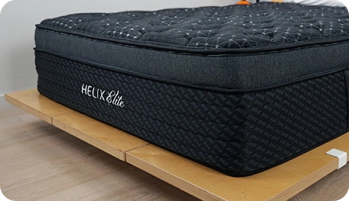 A dark charcoal gray quilted mattress on a wooden platform bed frame, with the brand name 'HELIX Elite' visible on the side.