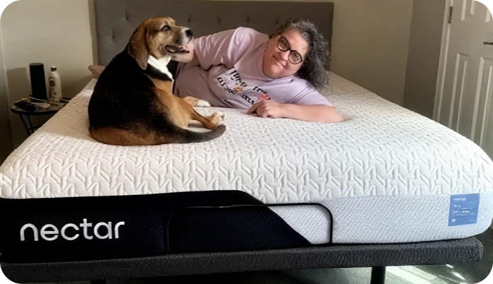 A person and a dog are lying on a Nectar mattress in a bedroom setting. The mattress has a white textured top and a black side panel with the brand name 'nectar' visible.