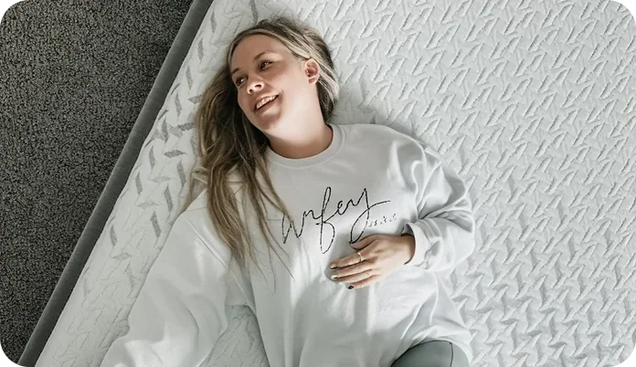 A woman lying on a textured white mattress, wearing a white sweatshirt with the words 'Wife of 10 Years' in black script.